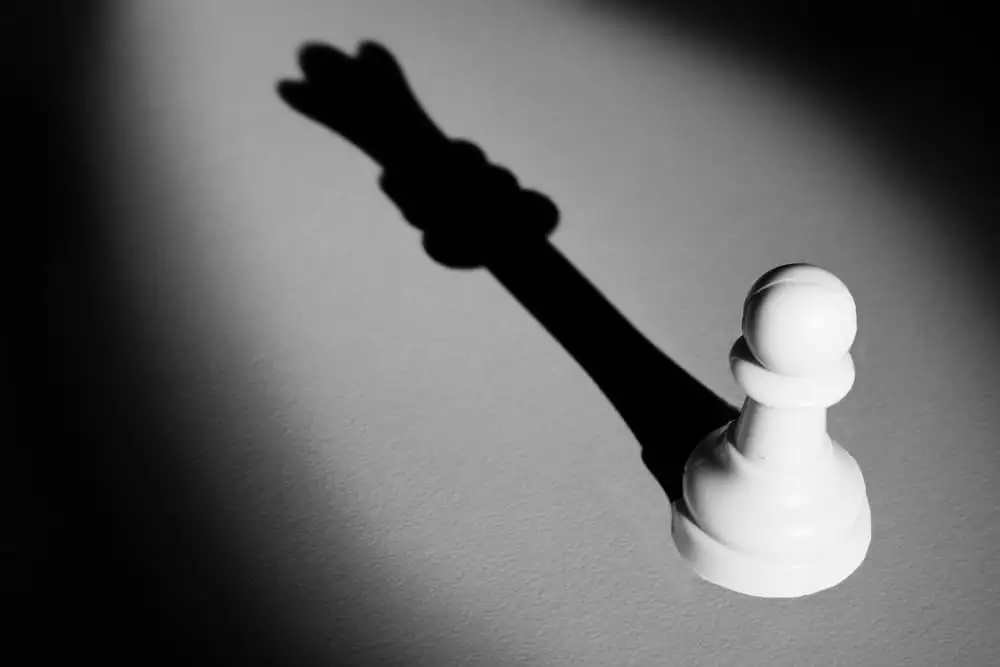 Chess pawn standing in a spotlight that make a shadow of queen
