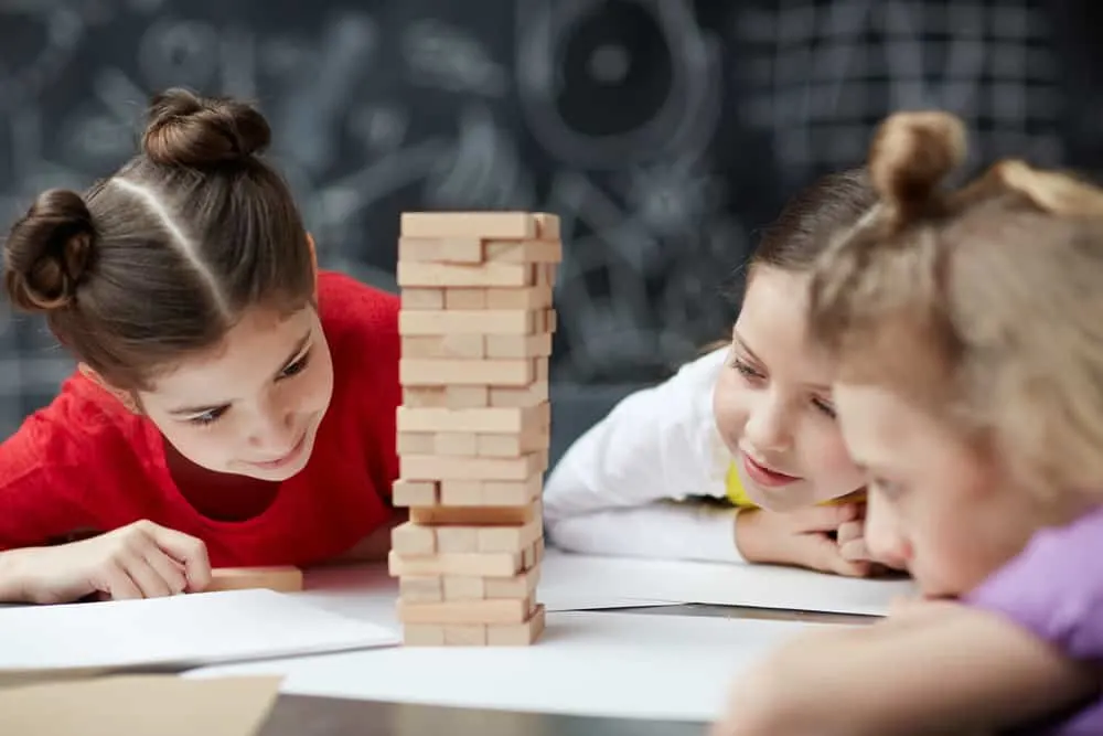 Friendly classmates building wooden-brick tower on desk jenga