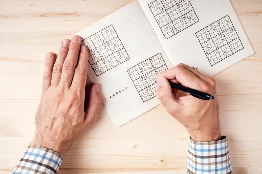 man solving sudoku puzzle on wooden office desk