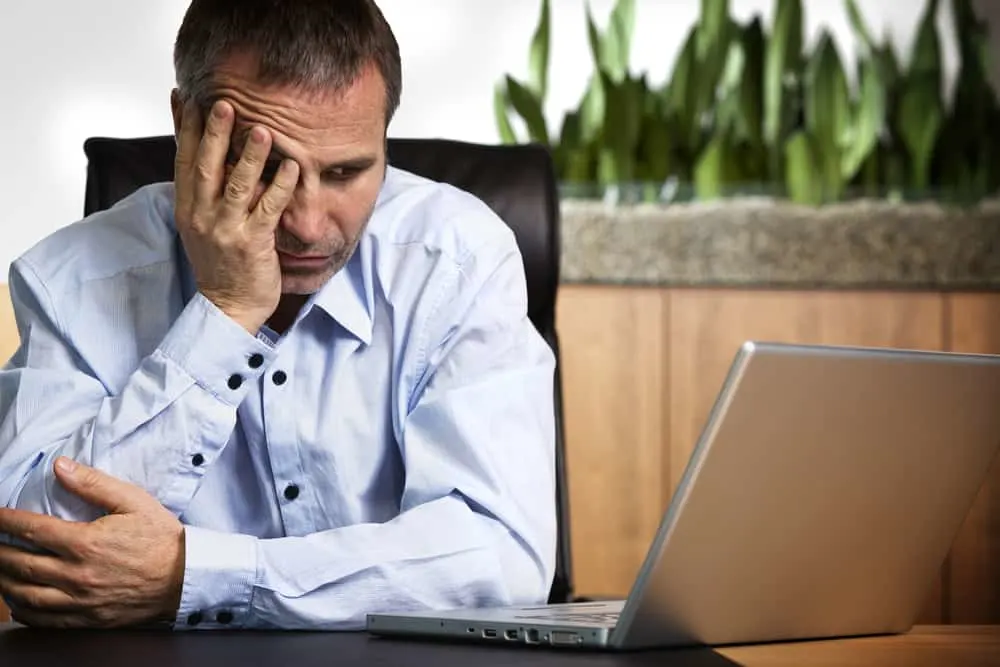 person in blue shirt sitting at office desk looking at laptop and being frustrated sudoku