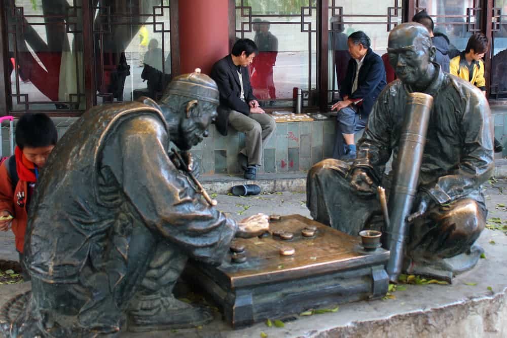 Two men playing checkers near the bronze sculpture depicting historical players