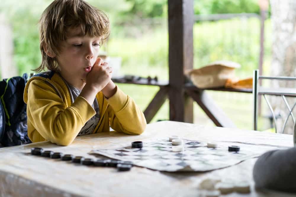a boy is playing checkers at a table on the summer porch