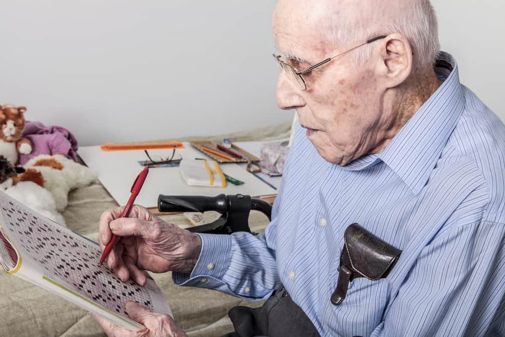 A elderly man sitting doing crosswords hobby