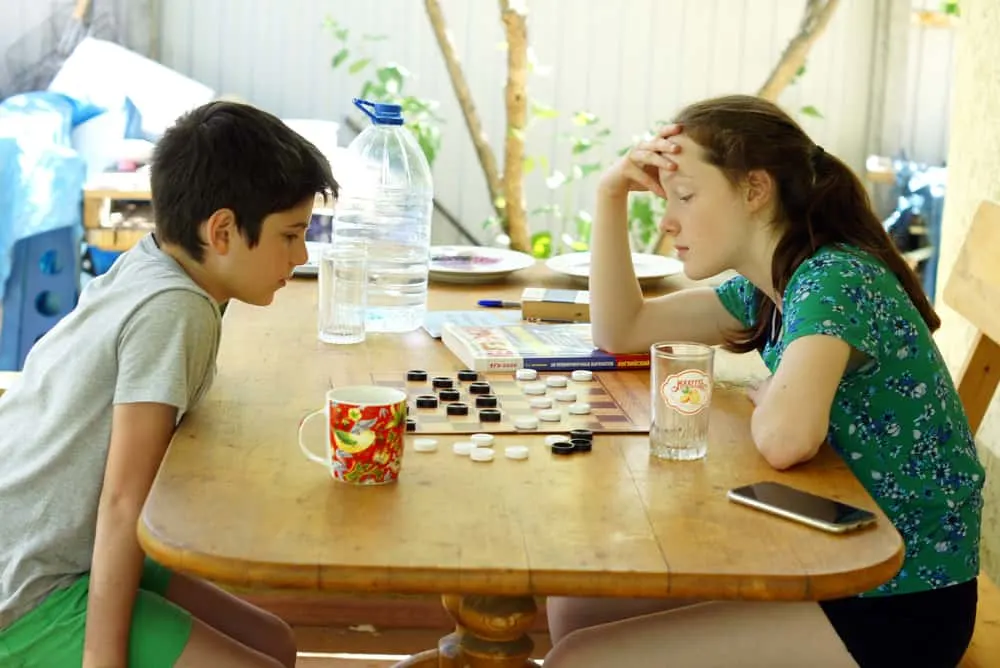 boy and girl play checkers at a table