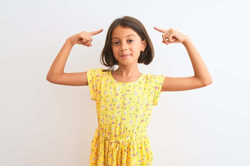 girl wearing yellow floral dress pointing to head, good memory