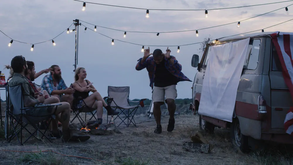 diverse group of people around bonfire in campsite and playing charades during sunset