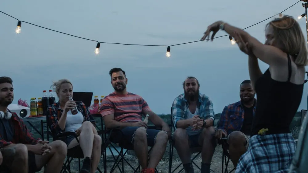 people chilling around bonfire in campsite and playing charades