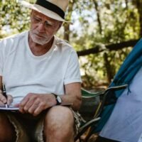 Senior man sitting in front of a tent and doing a word search puzzle