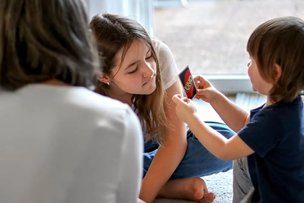 family playing UNO card board game sitting on carpet at home