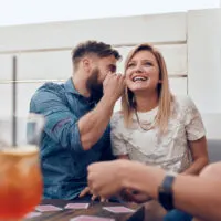 Man whispering something in woman's ears