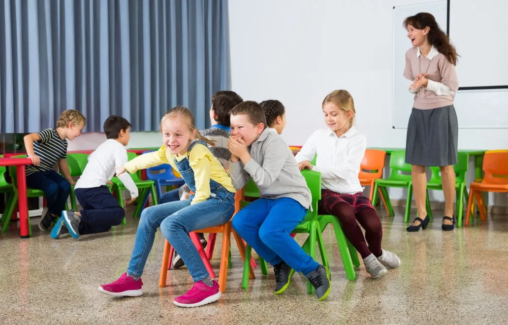 kids and female teacher playing musical chairs 