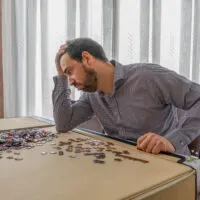 Bearded man in white and black shirt doing puzzle in his living room
