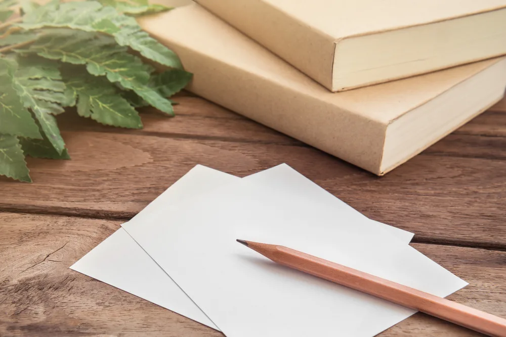 Pencil with paper and book on wooden table