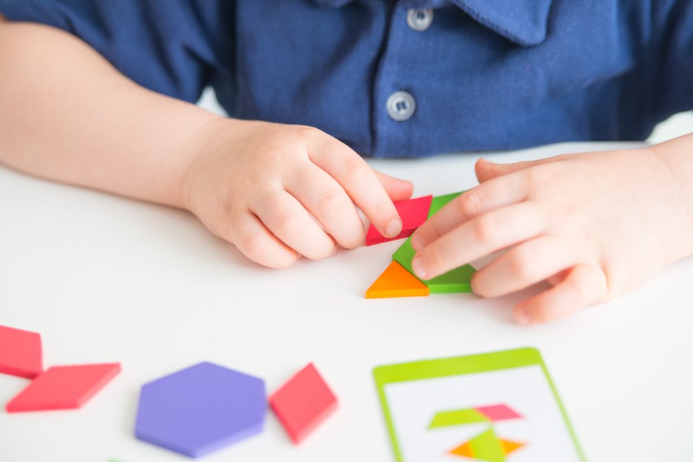 kid hands playing bright wooden tangram toy